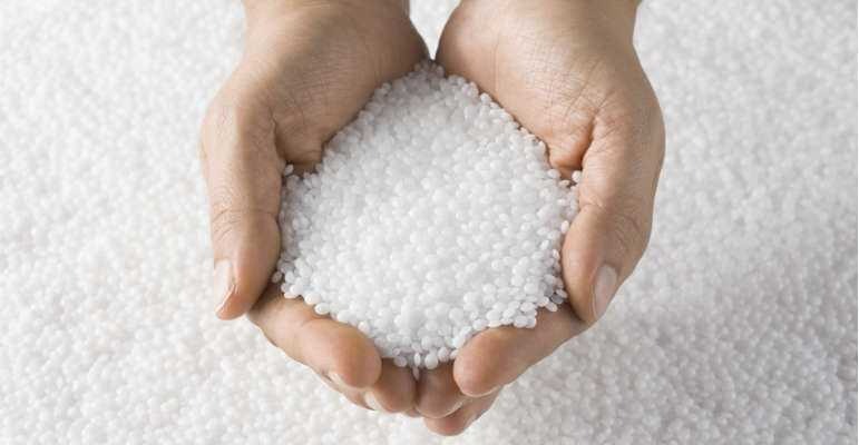 Hands holding small white plastic poly pellets used as weighted stuffing for toys.