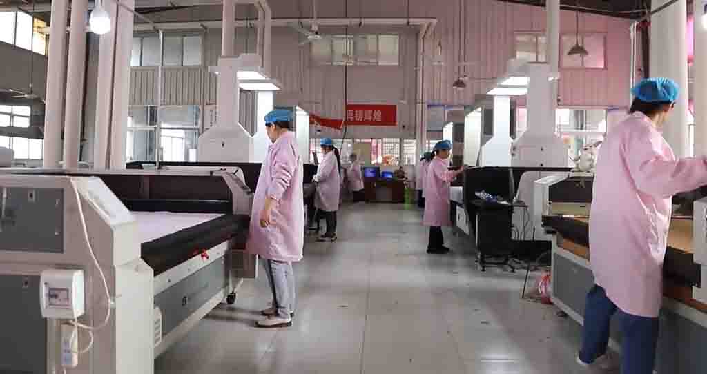 Workers in pink uniforms operating fabric cutting machines in plush toy factory.