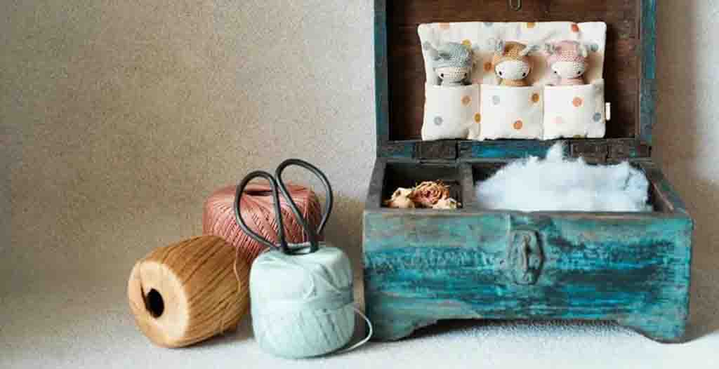 Wooden box with handmade fabric dolls, cotton stuffing, and spools of thread for making plush toys.