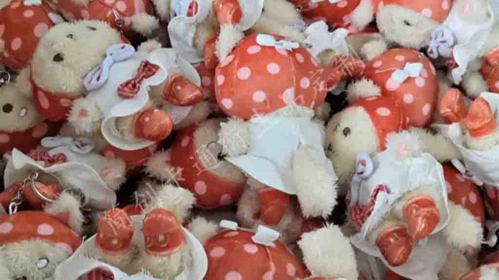 Pile of small teddy bear keychains dressed in red polka dot outfits with matching hats and shoes.
