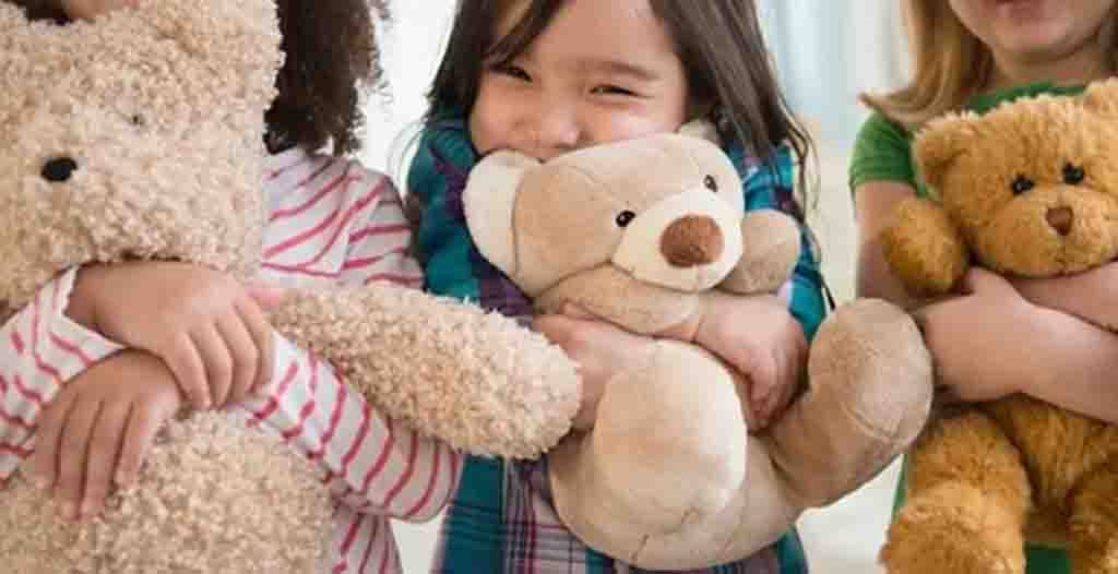 Three children hugging teddy bears with happy smiles.