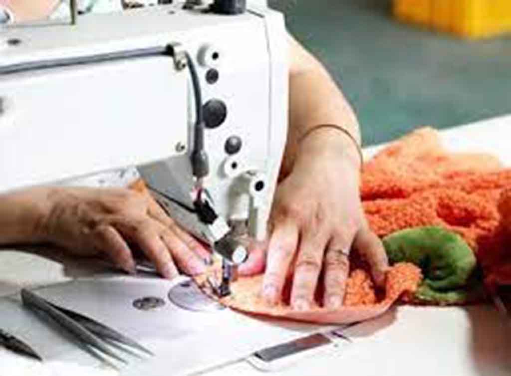 Worker sewing orange plush fabric using an industrial sewing machine.