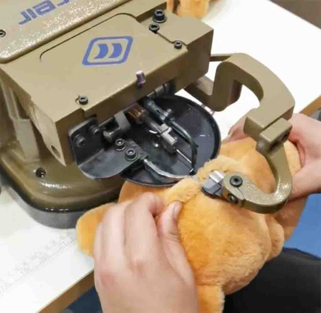 Worker using sewing machine to stitch closed a plush teddy bear during toy manufacturing.