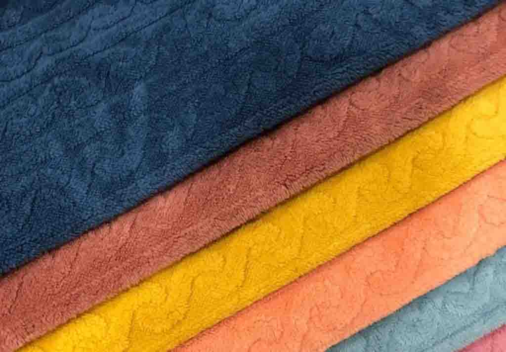 Close-up of colorful plush fabric swatches in blue, brown, yellow, pink, and gray, commonly used for making stuffed toys.