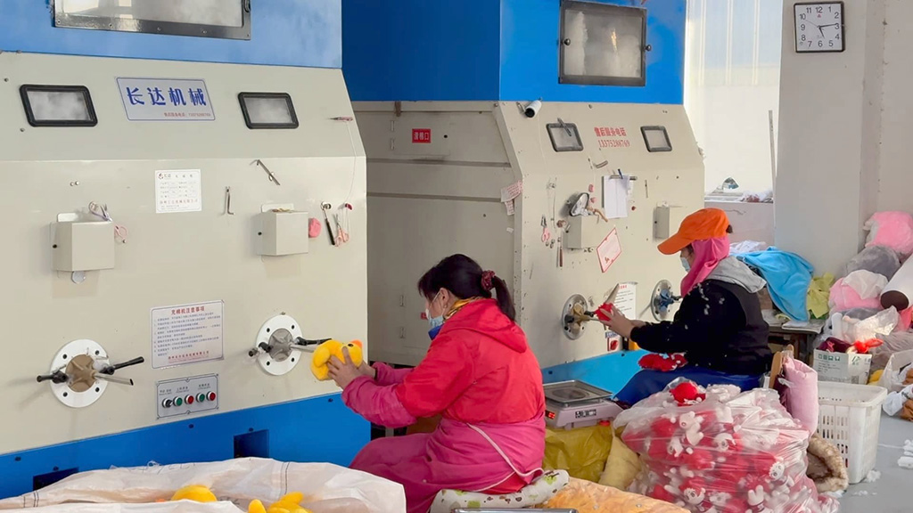 Workers using machines to stuff plush toys in factory.