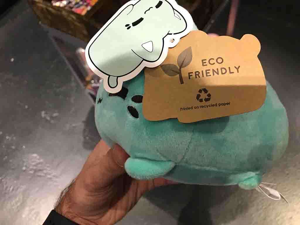 Hand holding eco-friendly plush toy with recycled paper tag.