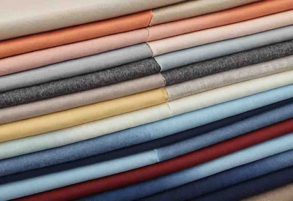 Neatly stacked colorful fabric rolls in various textures and shades.