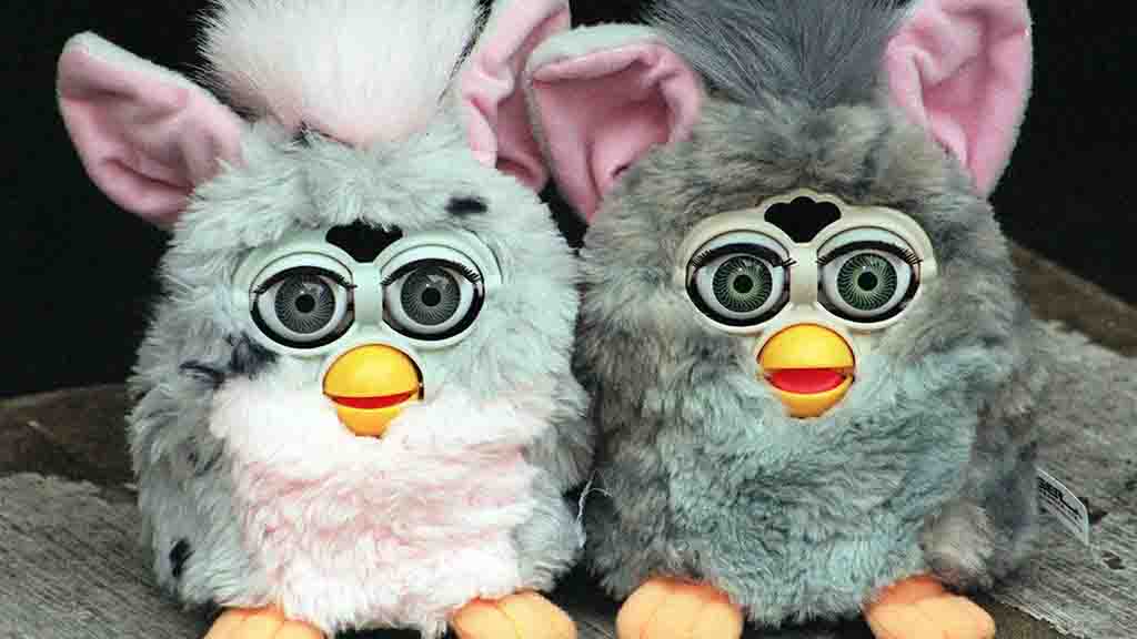 Two vintage Furby electronic plush toys with big eyes, gray fur, and pink ears sitting side by side.
