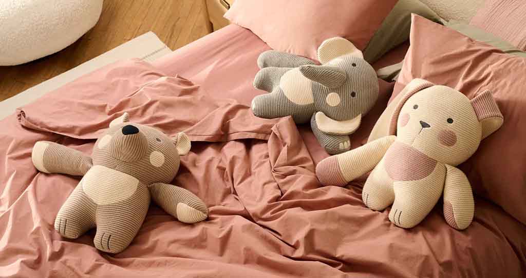 Bear, elephant, and dog corduroy plush toys on a pink bed.