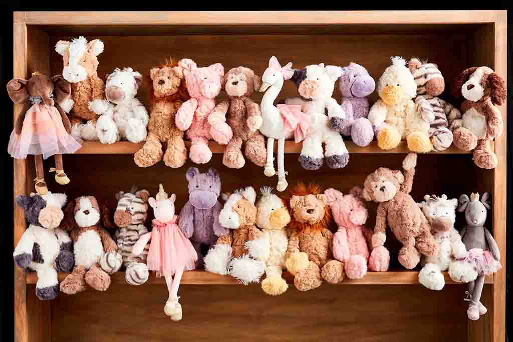 Collection of stuffed animals in various shapes and colors neatly arranged on a two-tier wooden shelf.