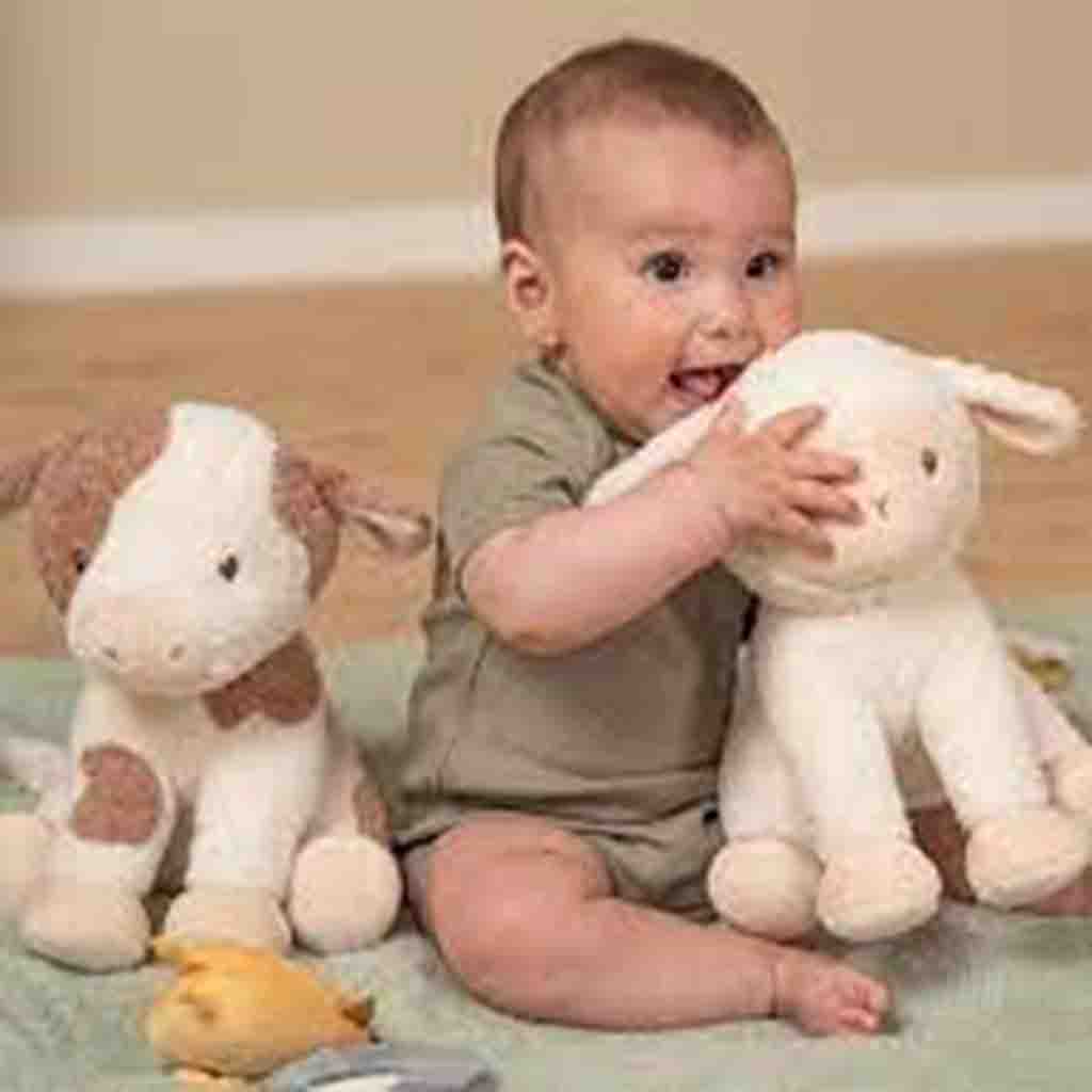 Smiling baby playing on the floor with two plush animal toys, one resembling a cow and the other a lamb.