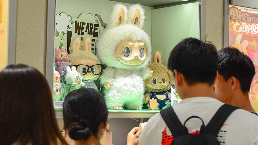 Shoppers viewing a store display of Labubu plush toys in various sizes and outfits, highlighting the collectible plush trend.