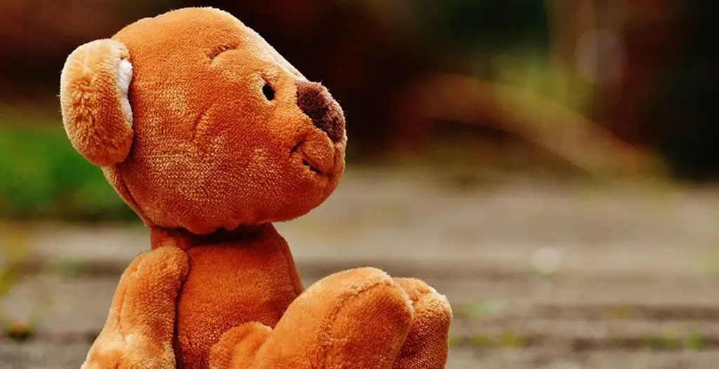 This is a photo of a plush teddy bear sitting on the ground outdoors.