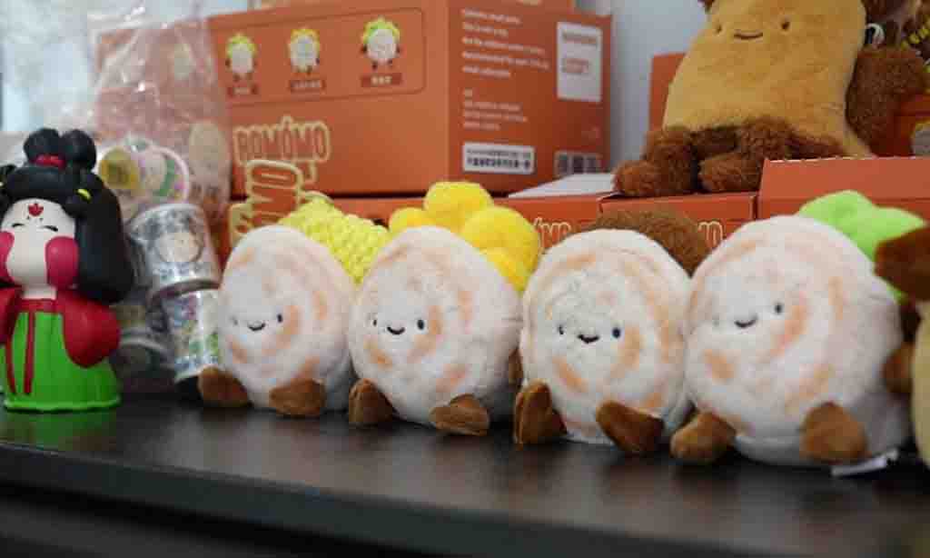 A row of cute dumpling-shaped plush toys with smiling faces displayed on a shelf, alongside other collectible plush and figurines.