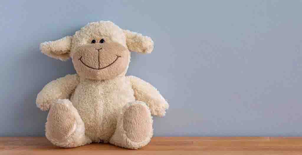 Cute sheep plush toy with big smile sitting on wooden surface against light blue wall.