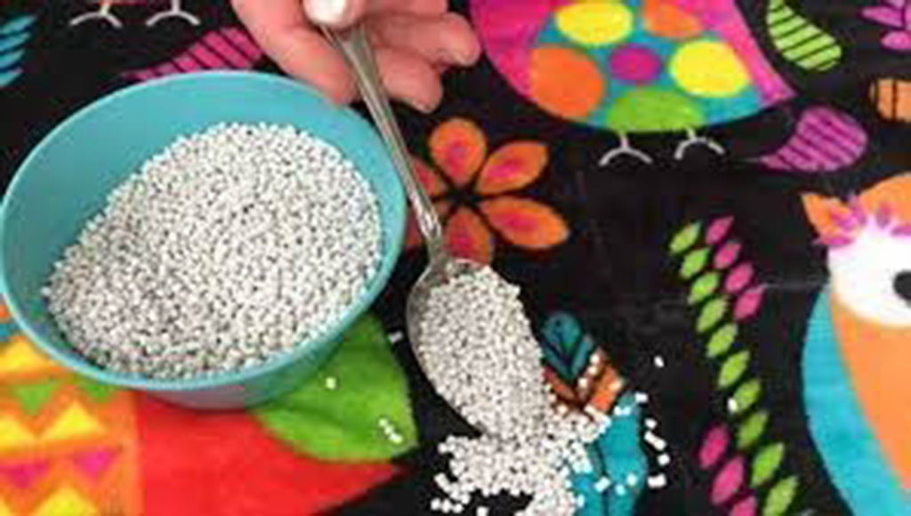 Hand scooping white plastic pellets from a bowl, used as filling material for making weighted stuffed animals.