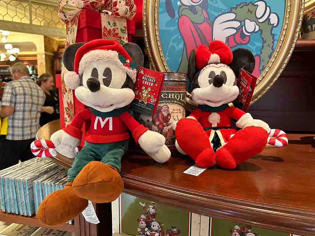 Mickey and Minnie Mouse plush toys in festive Christmas outfits displayed on a wooden shelf with holiday decor.