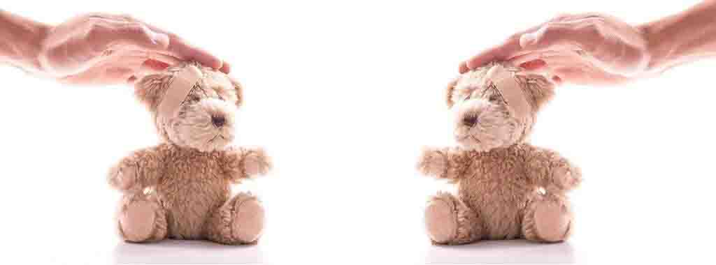 Two brown teddy bears with bandages on heads being gently patted by hands on white background.