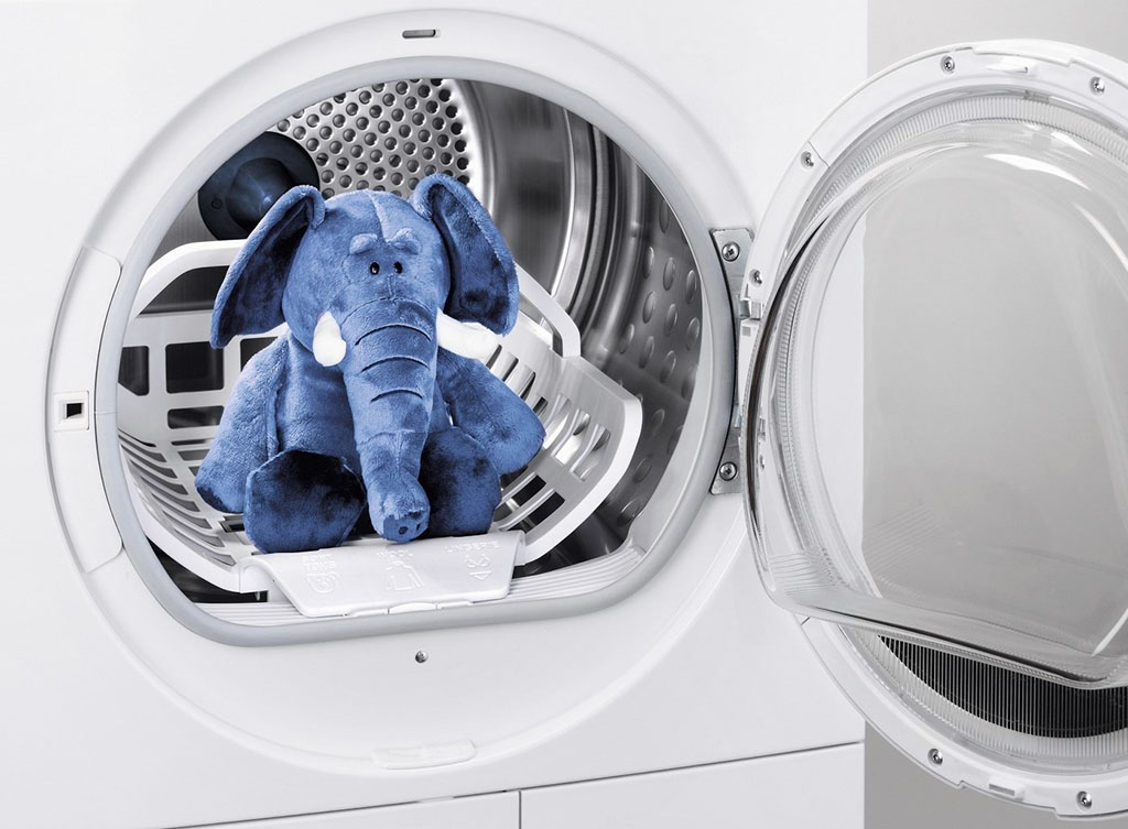 Blue stuffed elephant toy placed inside a washing machine drum for cleaning.
