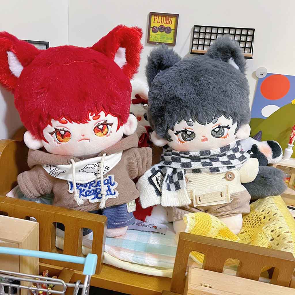 Two anime-style plush dolls with fox ears, wearing hoodies and scarves, sitting on a wooden bed in a miniature room setting.