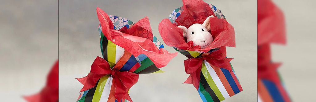 Stuffed animal wrapped in colorful striped gift paper with red tissue paper and tied with a big red bow.