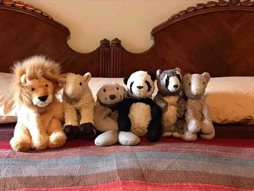 A group of plush animal toys including a lion, sheep, panda, and bear neatly arranged on a bed.