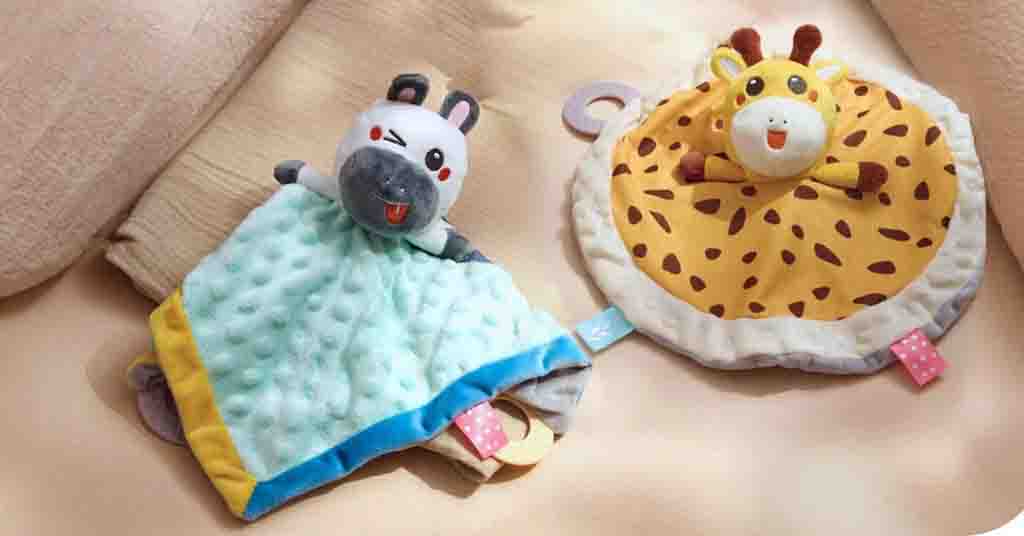 Two baby comfort plush toys, one zebra with a soft blue blanket and one giraffe with a round spotted blanket.