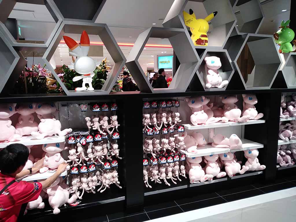 A retail store display featuring shelves filled with Pokémon plush toys, including Mew, Pikachu, and other characters, arranged in hexagonal shelves.