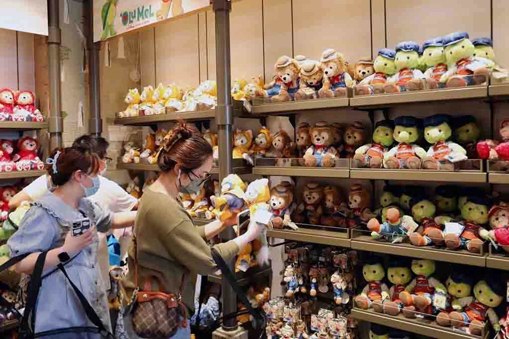 Customers wearing masks browsing and selecting plush toys from shelves filled with teddy bears and character plushies in a toy store.