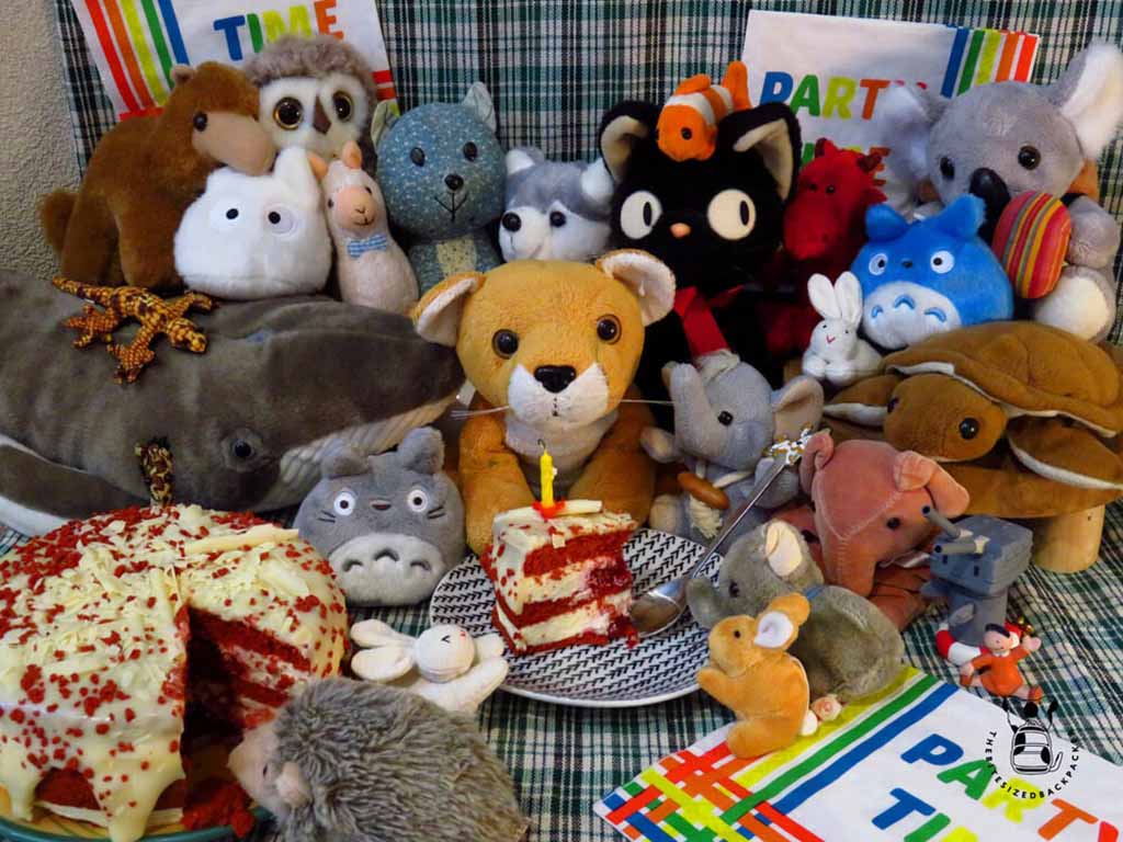 A group of plush toys gathered around a table with cake slices and party decorations, creating a fun plushie party atmosphere.