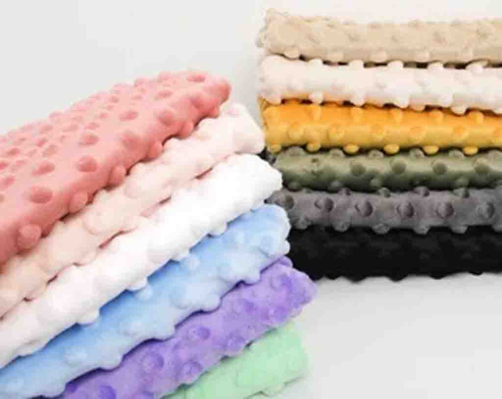 Stacked minky dot fabric pieces in multiple colors including pink, white, blue, purple, yellow, green, gray, and black.