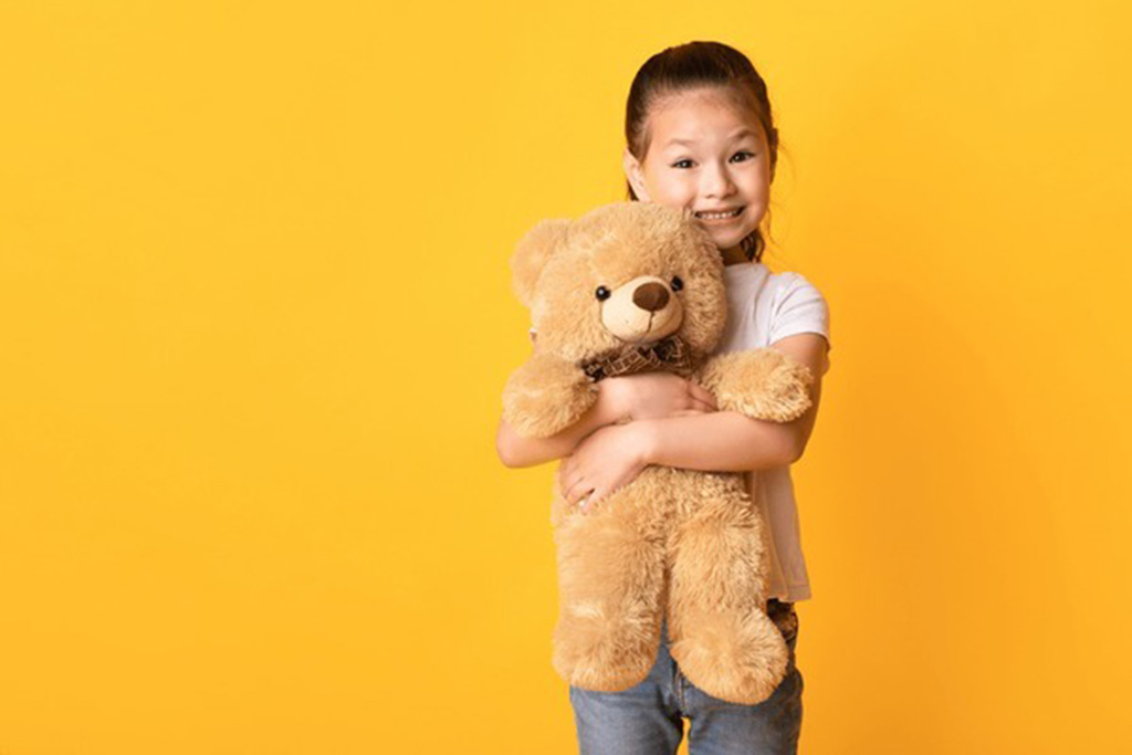 Smiling young girl hugging a fluffy teddy bear against a bright yellow background.