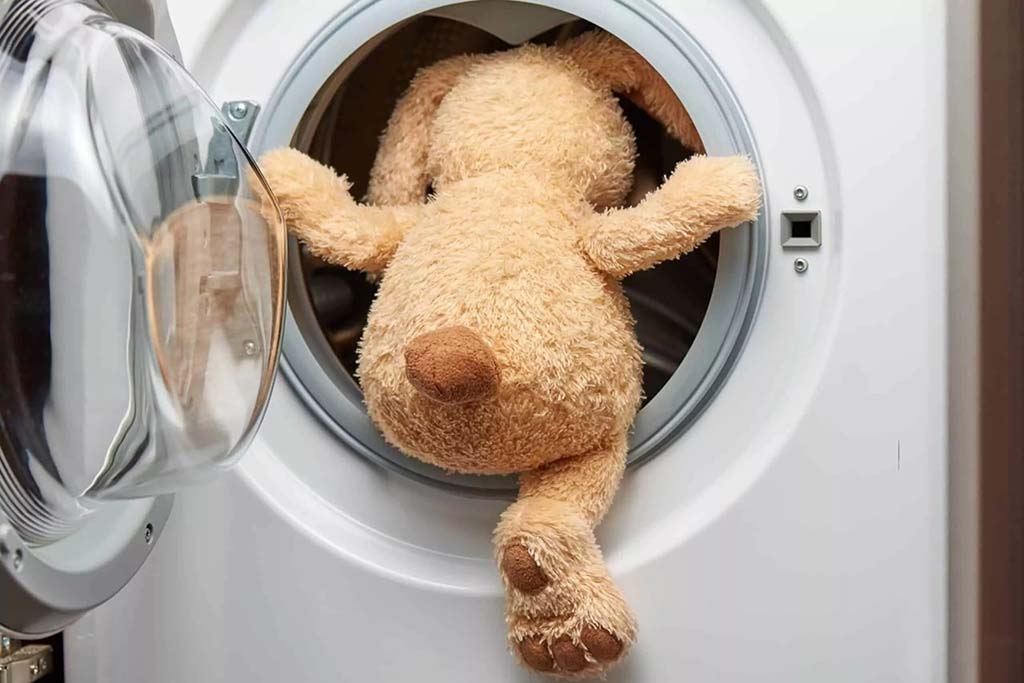 Stuffed dog toy placed inside a front-loading washing machine for cleaning.