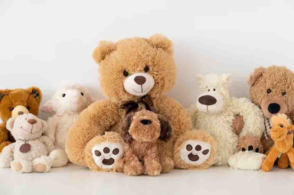Collection of soft stuffed animals including teddy bears, a dog, and a camel arranged together against a white background.