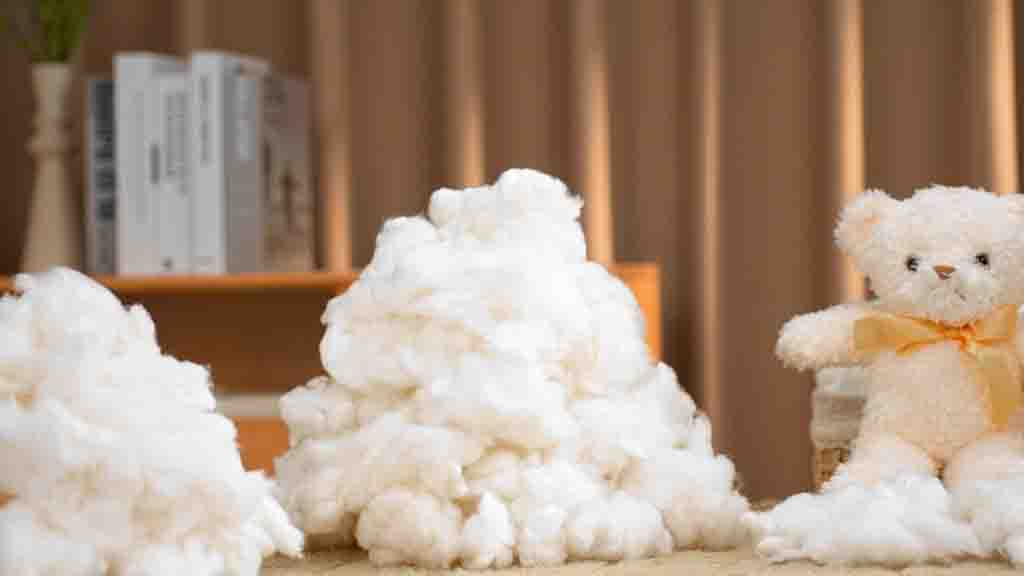Soft white cotton stuffing piled beside a teddy bear with orange ribbon sitting on a table indoors.