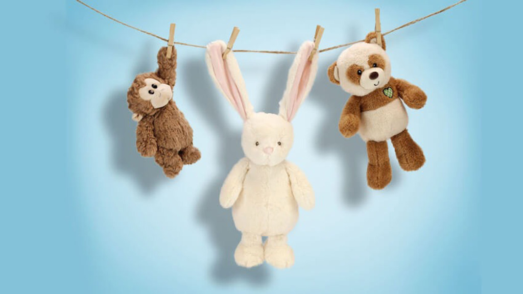 Plush monkey, bunny, and bear hanging on a clothesline with clothespins against a blue background for air drying.