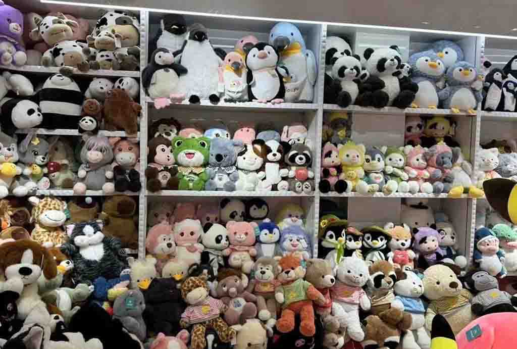 Shelves filled with assorted stuffed animals including pandas, penguins, frogs, bears, and giraffes in a wholesale plush toy store.
