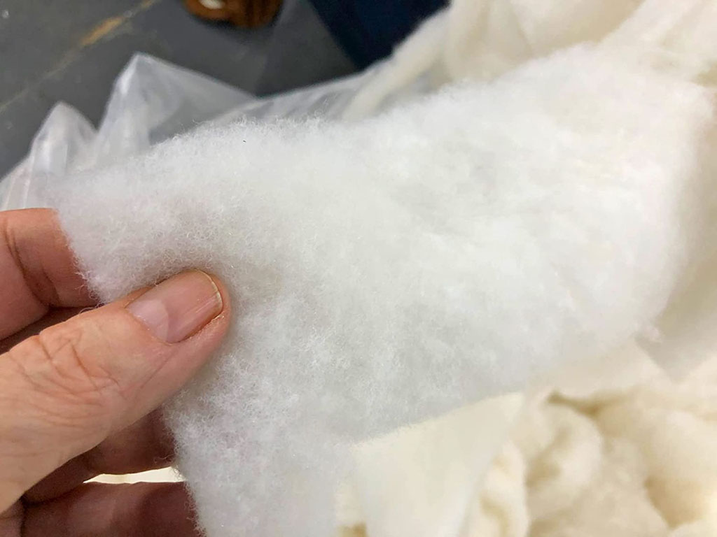 Hand holding a sheet of white batting material, often used as stuffing or lining in plush toys and stuffed animals for structure and softness.