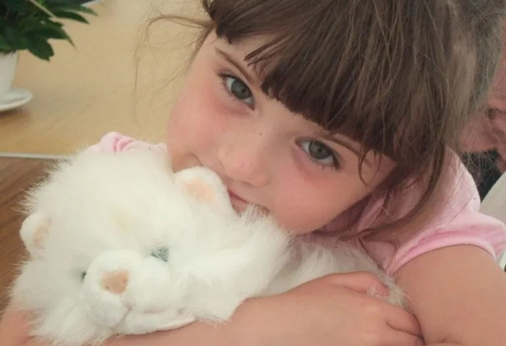 Young girl hugging a fluffy white stuffed animal cat for comfort.