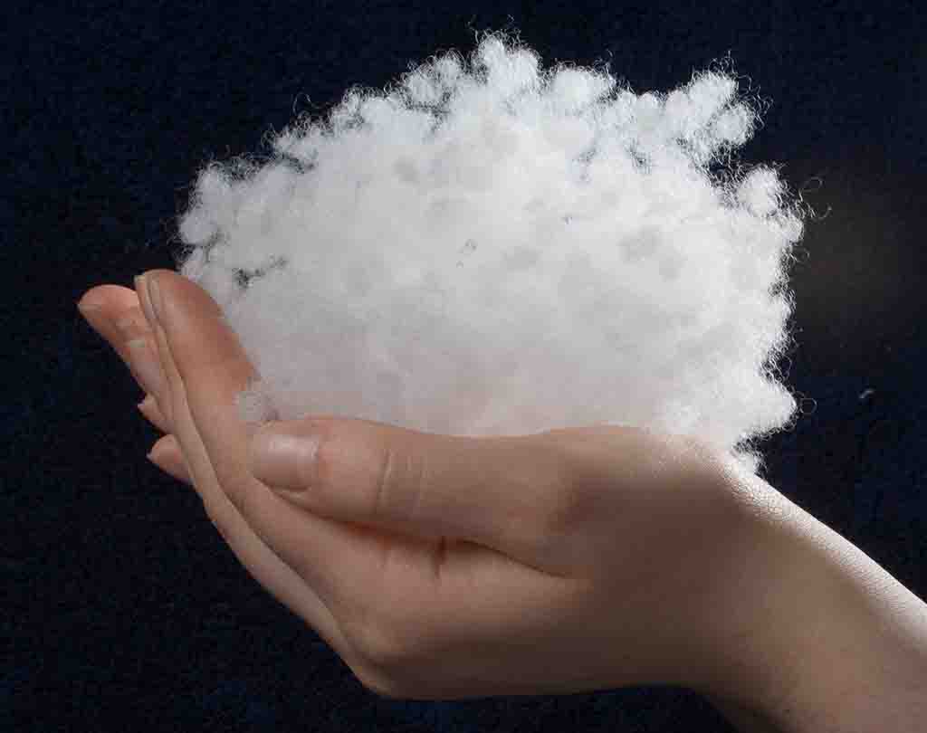 Hand holding fluffy white polyester fiberfill stuffing against dark background.
