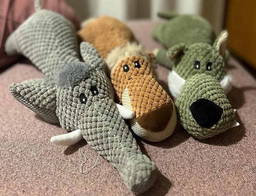 Three textured plush dog toys shaped like an elephant, a brown animal, and a green dog, designed for chewing and play.