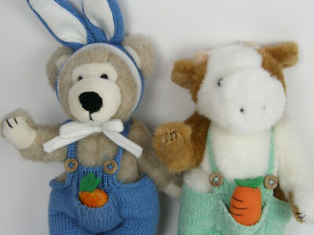 Stuffed bear with bunny ears and stuffed cow toy dressed in colorful overalls with carrot designs.
