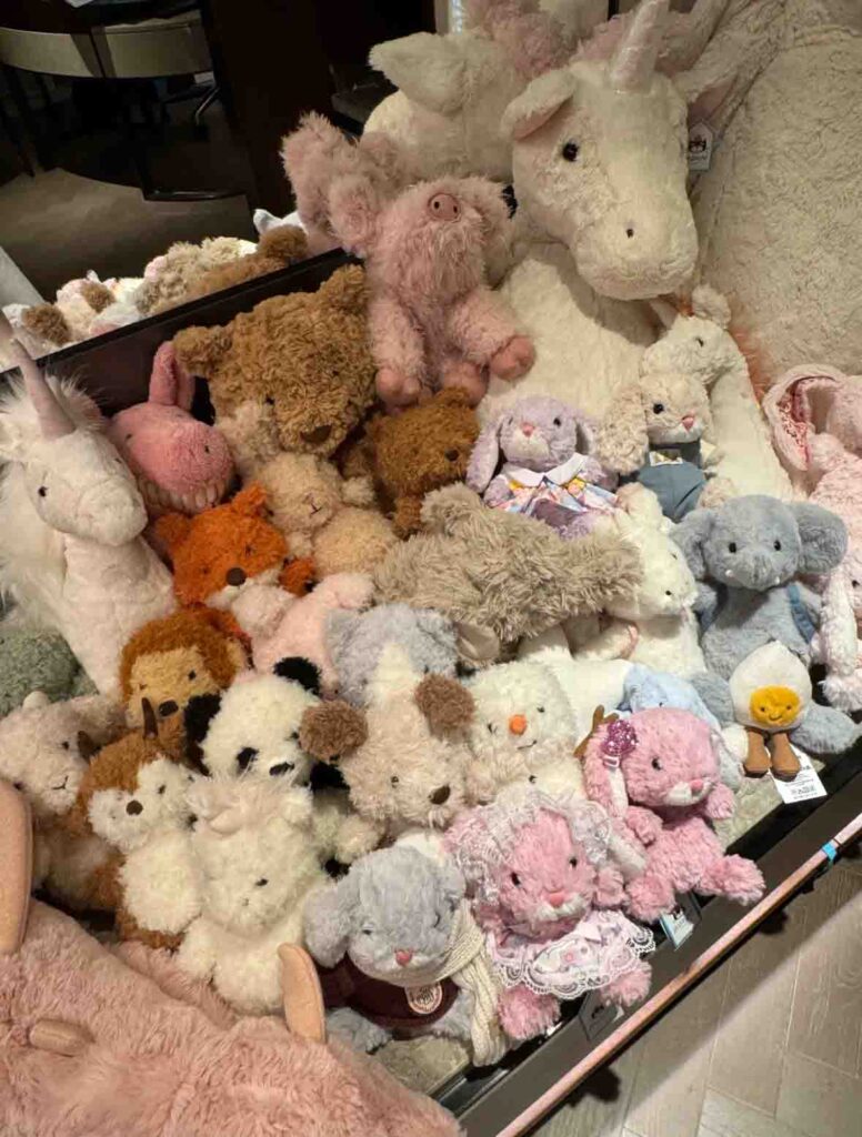 Assorted plush toys including bears, bunnies, pandas, and unicorns displayed together in a store.