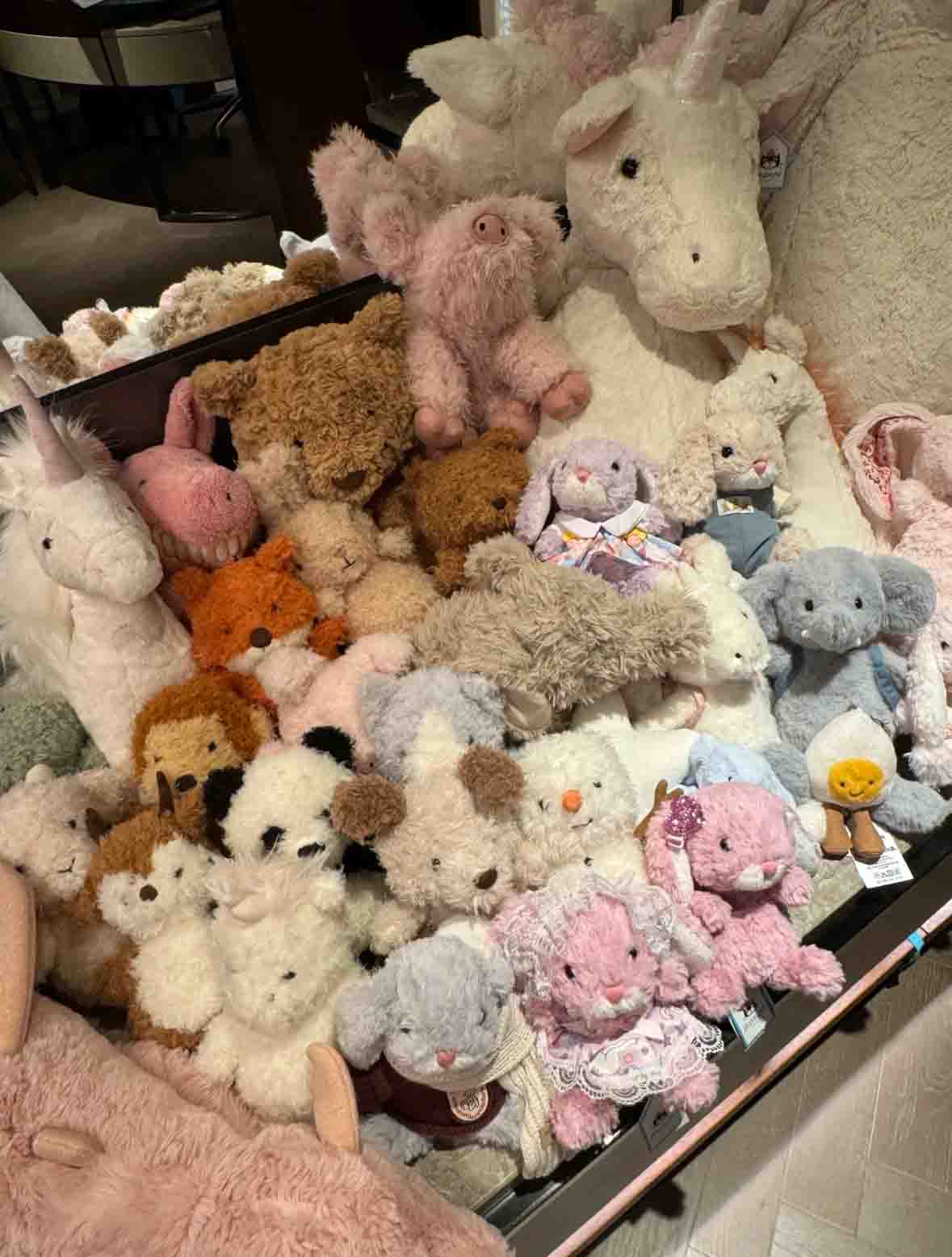 Assorted plush toys including bears, bunnies, pandas, and unicorns displayed together in a store.
