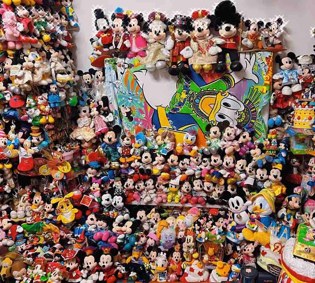 Large display of Mickey, Minnie, Donald, and Disney-themed plush toys in colorful costumes arranged on shelves and walls.
