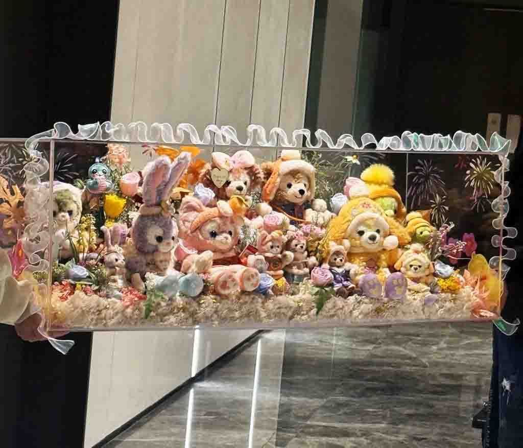 Display of limited edition Disney plush toys including Duffy and friends dressed in seasonal costumes with floral decorations and fireworks background.