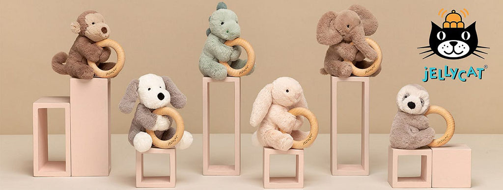 Collection of Jellycat plush animals holding wooden teething rings displayed on pastel stands with the Jellycat logo.