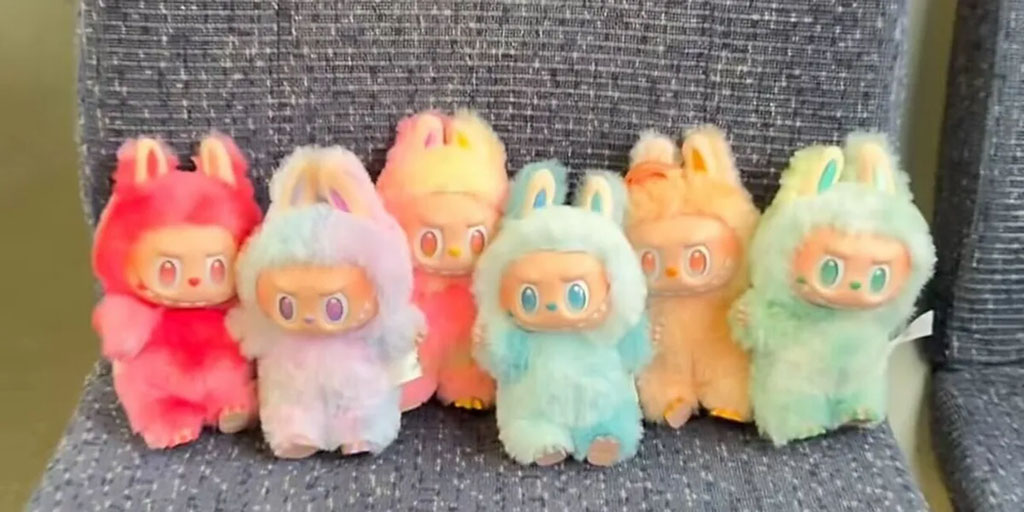 Row of colorful Labubu plush toys in bunny costumes sitting on a fabric seat.