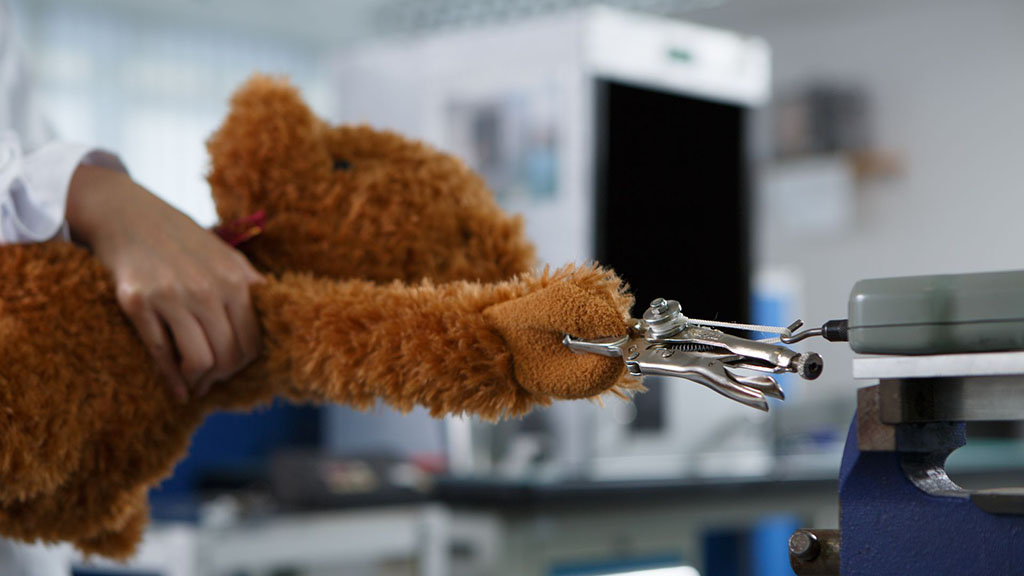 Laboratory technician testing a teddy bear’s durability and seam strength using clamps to ensure toy safety compliance.