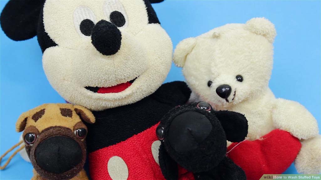 A collection of plush toys including a large Mickey Mouse, a white teddy bear, a small brown dog, and a black lamb against a blue background.